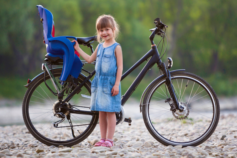 dziewczynka stoi przed rowerem z fotelikiem dla dziecka